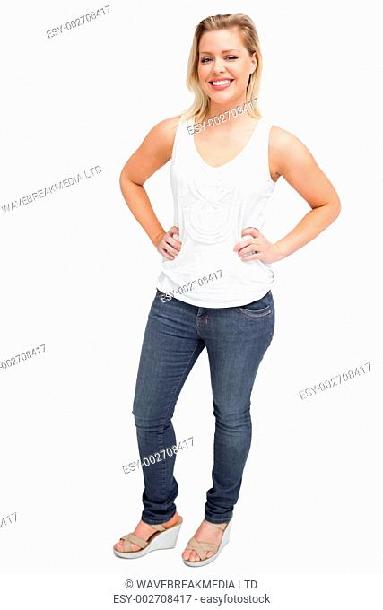Smiling blonde woman placing her hands on her hips against a white background