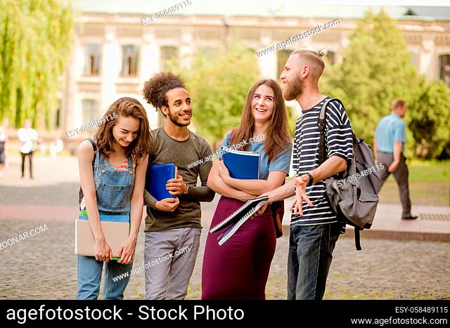 College friends standing, laughing in campus. Young people having fun in the university park