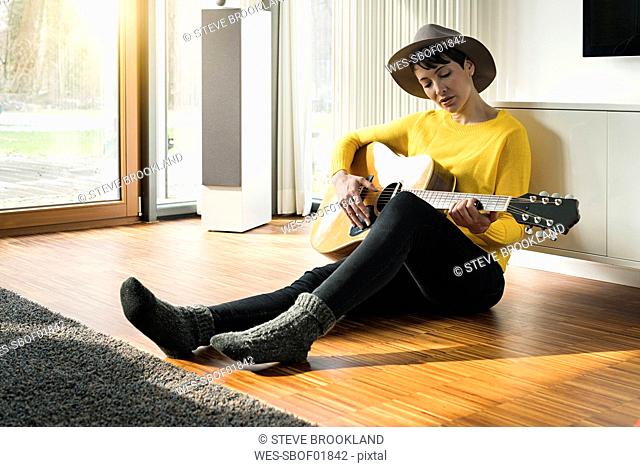 Woman sitting on the floor of living room playing guitar