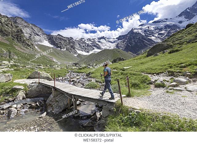 A trekker crosses a small wooden bridge near the Zamboni Zappa refuge at the foot of the East face of Monte Rosa Massif (Macugnaga, Anzasca Valley