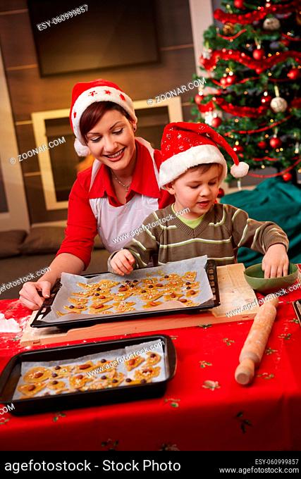 Smiling mum and small son decorating christmas cake together at table