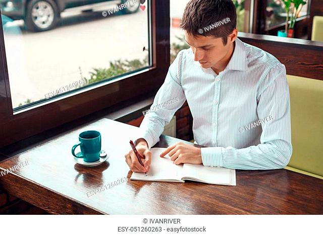 Handsome young businessman working and writing something in notebook. Confident young male with cup of coffee working outdoors