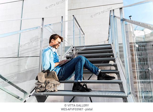 Casual businessman sitting on stairs using laptop