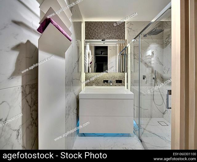 Bathroom in a modern style with light tiles on the walls and the floor. There is a white sink with a chrome faucet and a mirror, a shower with glass door
