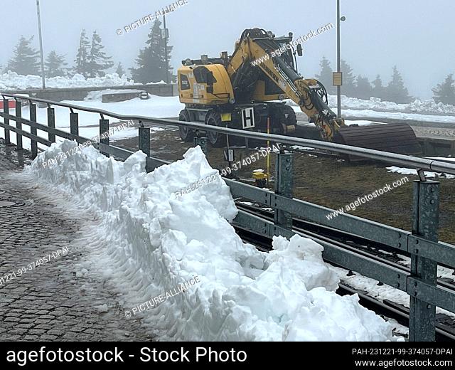21 December 2023, Saxony-Anhalt, Schierke: Brocken station with mountains of snow. An excavator stands in the track bed. Harzer Schmalspurbahnen GmbH has...
