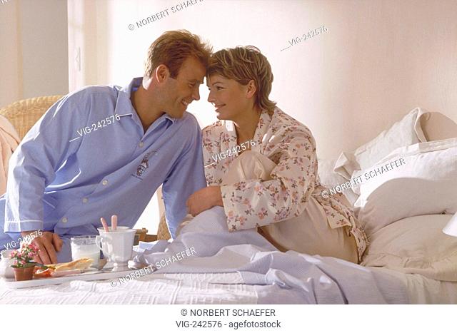 portrait, indoor, half-figure, young blond couple wearing pyjama sit on a Sunday morning at breakfast in bed  - GERMANY, 07/03/2005