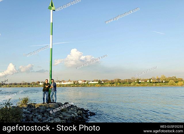 Son and father by pole standing on rock against river and sky