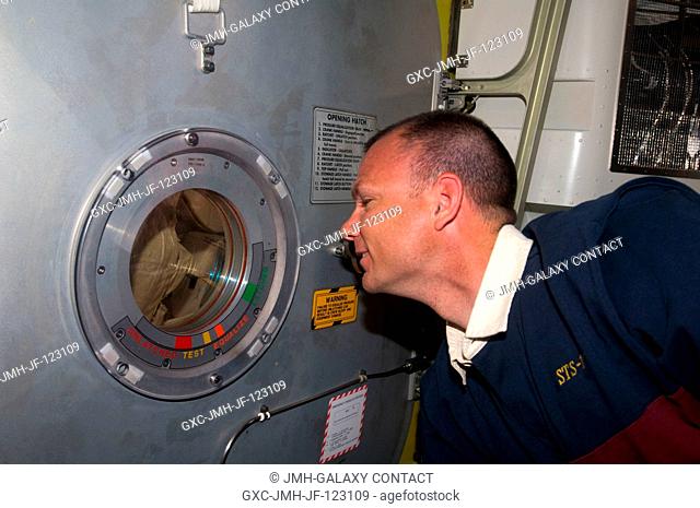 Astronaut Tony Antonelli, STS-119 pilot, watches his crewmates through a small window on the hatch door in the Quest Airlock of the International Space Station...