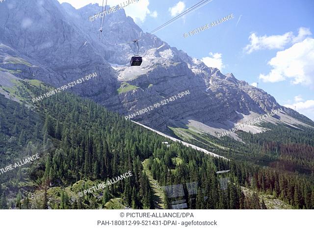 19 July 2018, Germany, Zugspitze: A cable car of the cable car Zugspitze can be seen at the mountain massif of the Zugspitze from the valley station