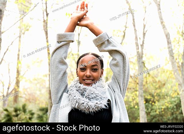 Smiling teenage girl with arms raised wearing scarf and trench coat