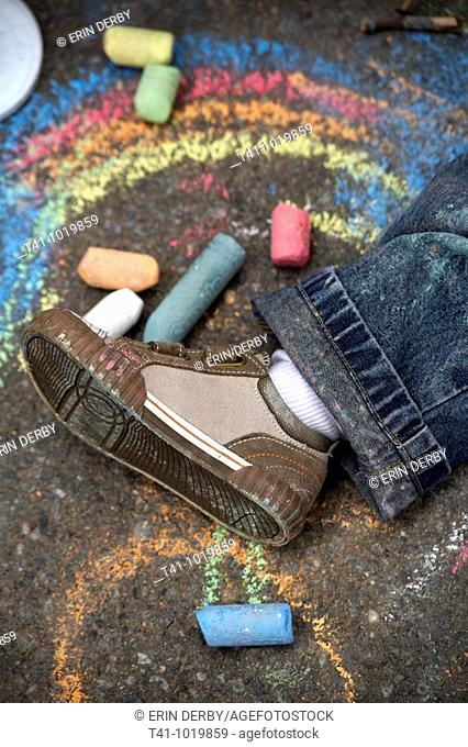 An overhead photograph of a 2 year old boy's shoe on a sidewalk surrounded by chalk and drawings