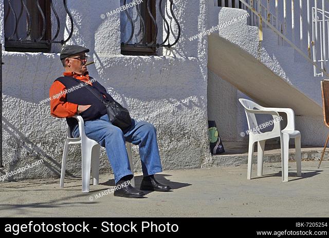 Man with cap and waistcoat sitting on chair smoking cigar, Villaricos, Andalucia, Spain, Europe