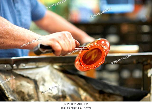 Glassblower in workshop shaping molten glass material with hand tools