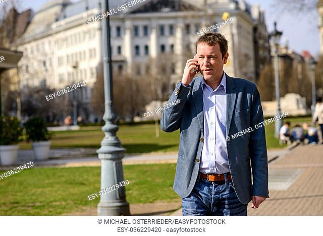 A middle age businessman walking in a park while talking on his phone