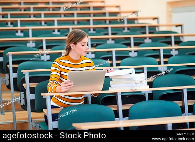 Female student taking notes from a book at school calssroom. Young woman sitting at table doing assignments