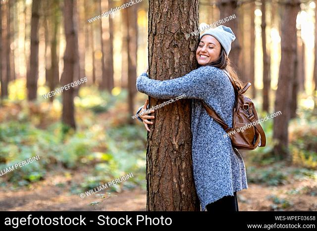 Happy female hiker embracing tree while hiking in Cannock Chase woodland during winter