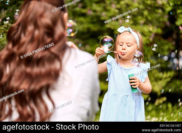 mother with daughter blowing soap bubbles at park