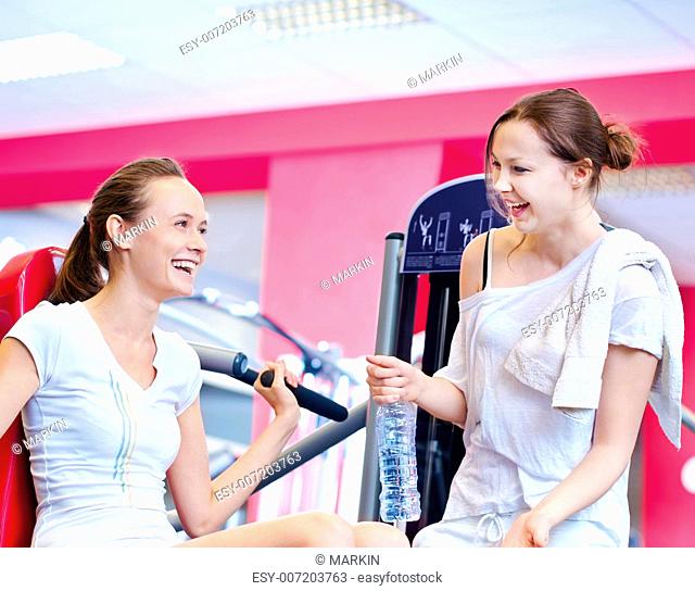 Woman doing fitness training on a butterfly machine with weights in a gym with friend