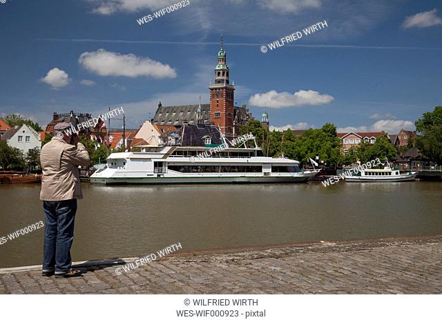 Germany, Lower Saxony, Leer, senior man taking a picture of the city and the ships with his smartphone