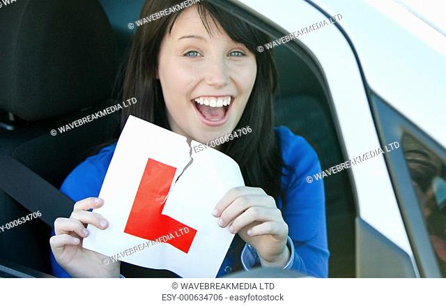 Happy brunette teen girl sitting in her car tearing a L-sign after having her drivers licence