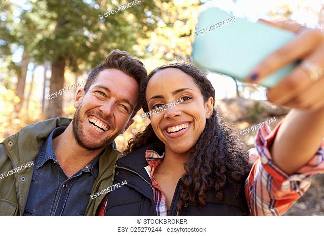 Laughing mixed race couple taking a selfie in a forest