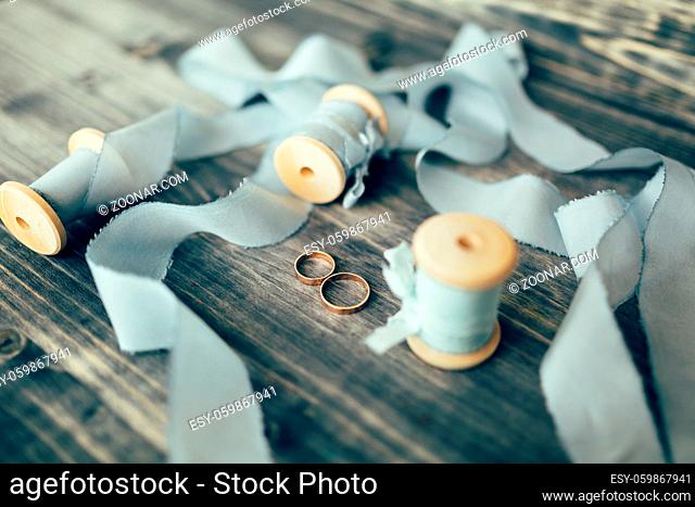 Gold wedding rings on a wooden surface with spools with gray silk ribbons. High quality photo