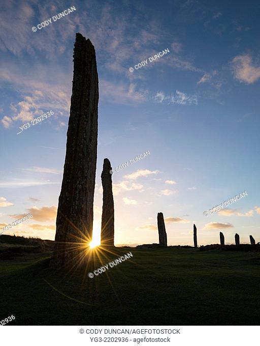 Setting sun shines behind standing stone at Ring of Brodgar, Orkney, Scotland