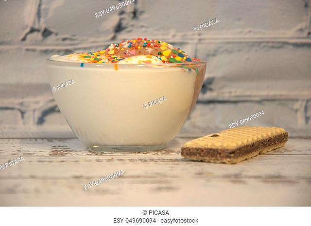 A cup of ice cream with a scattering and a vyflya lie on a wooden table. Still life
