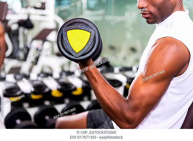 Making his biceps perfect. Cropped image of young African man training with dumbbell in gym
