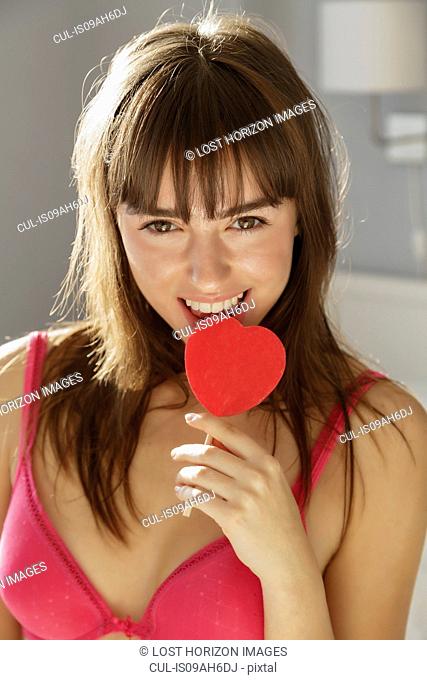 Young woman biting heart shape lollipop