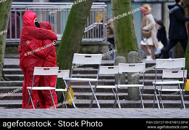27 January 2022, Hamburg: Two women in red full-body suits embrace each other on Gerhart-Hauptmann-Platz in the city center during a performance commemorating...