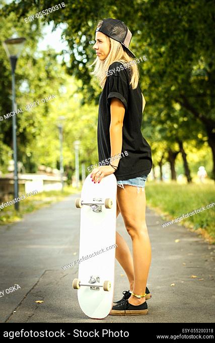 girl with a white skateboard stands and poses on a summer day