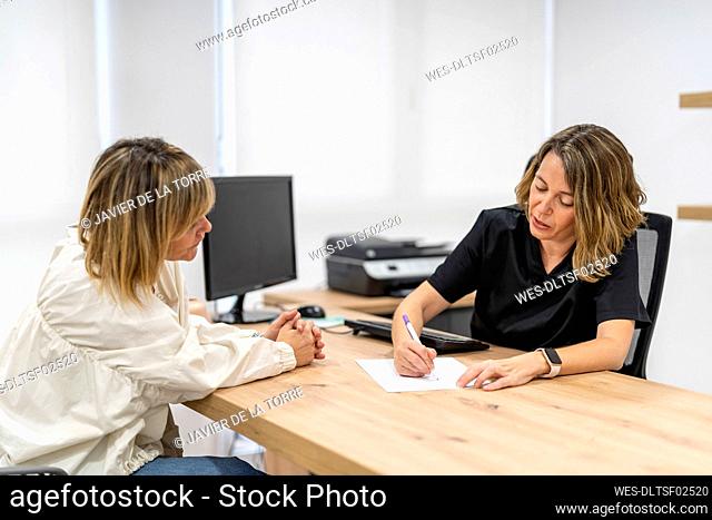 Doctor writing on paper while talking to patient in clinic