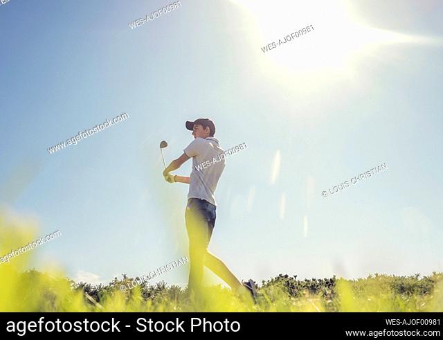 Teenage boy playing golf against clear sky during sunny day