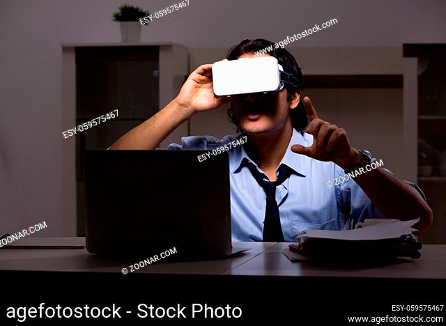 Young employee with virtual glasses at night in the office
