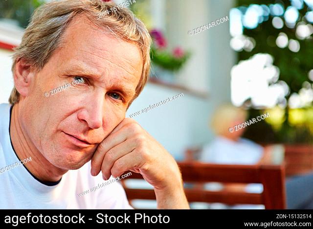 Nachdenklicher alter Mann sitzt vor seinem Haus