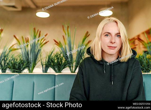 Blond businesswoman with hooded shirt sitting in coworking office