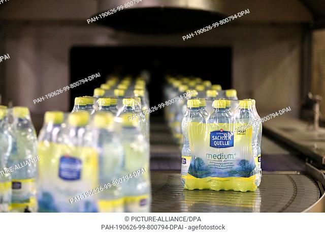 24 June 2019, Saxony, Eilenburg: 6-pack carriers with Ileburger mineral water with lemon taste run through the filling plant at Sachsenquelle GmbH