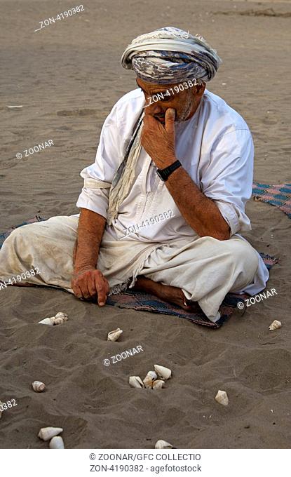 Omanischer Mann überlegt den nächsten Zug im Hawalis - Spiel mit Muscheln im Sand, omanische Variante des Mancala-Spiels