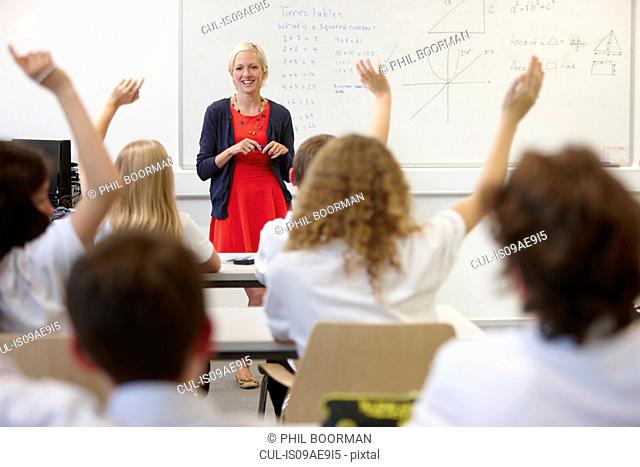 Female teacher and class with hands raised
