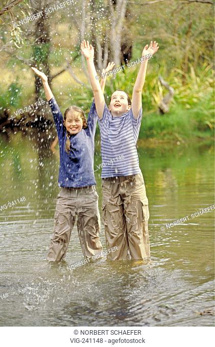 portrait, 2 laughing girls, 12 years, with long hair standing with wet t-shirt and trousers up to the knees in a rivulet  - GERMANY, 25/01/2004