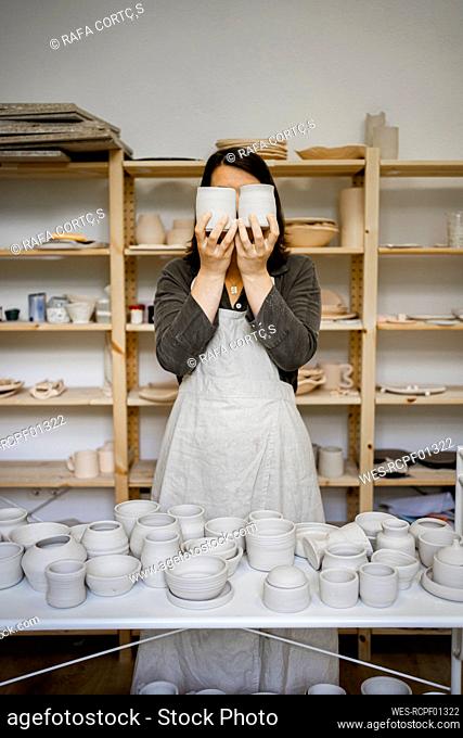Female potter covering face with ceramics in workshop