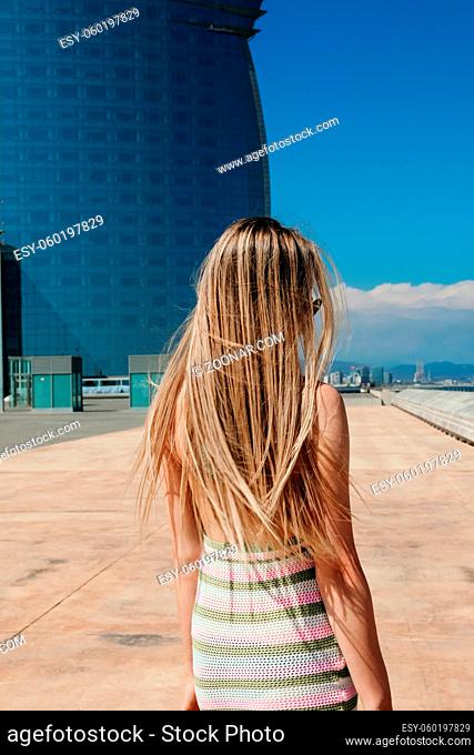 Vertical shot from back of long-haired woman walking on the beach in sunny day. High quality photo
