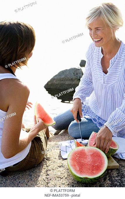 Two women eating watermelon by the sea, Sweden