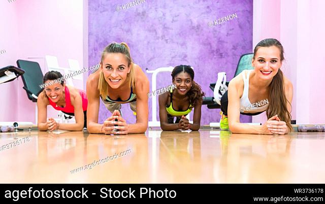 Low-angle front view of four women smiling while practicing forearm plank position for core strength in a trendy fitness club for ladies only