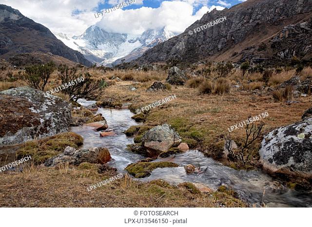 Mountain stream with valley and snow-capped mountains beyond, blue sky, Cordilleras, Peru