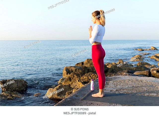 Young woman practicing yoga on the beach, doing prayer position