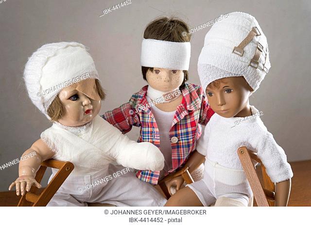 Three dolls sitting, bandages on head, leg splint, crutches, eye patch, arm and shoulder bandage, neck brace