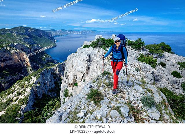 A young woman with trekking gear hiking along the mountainous coast above the sea, Golfo di Orosei, Selvaggio Blu, Sardinia, Italy, Europe