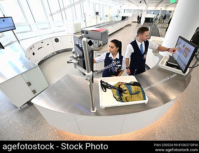 24 May 2023, Bavaria, Munich: ILLUSTRATION - Two security checkpoint employees check baggage in one of a total of five new installations at Munich Airport
